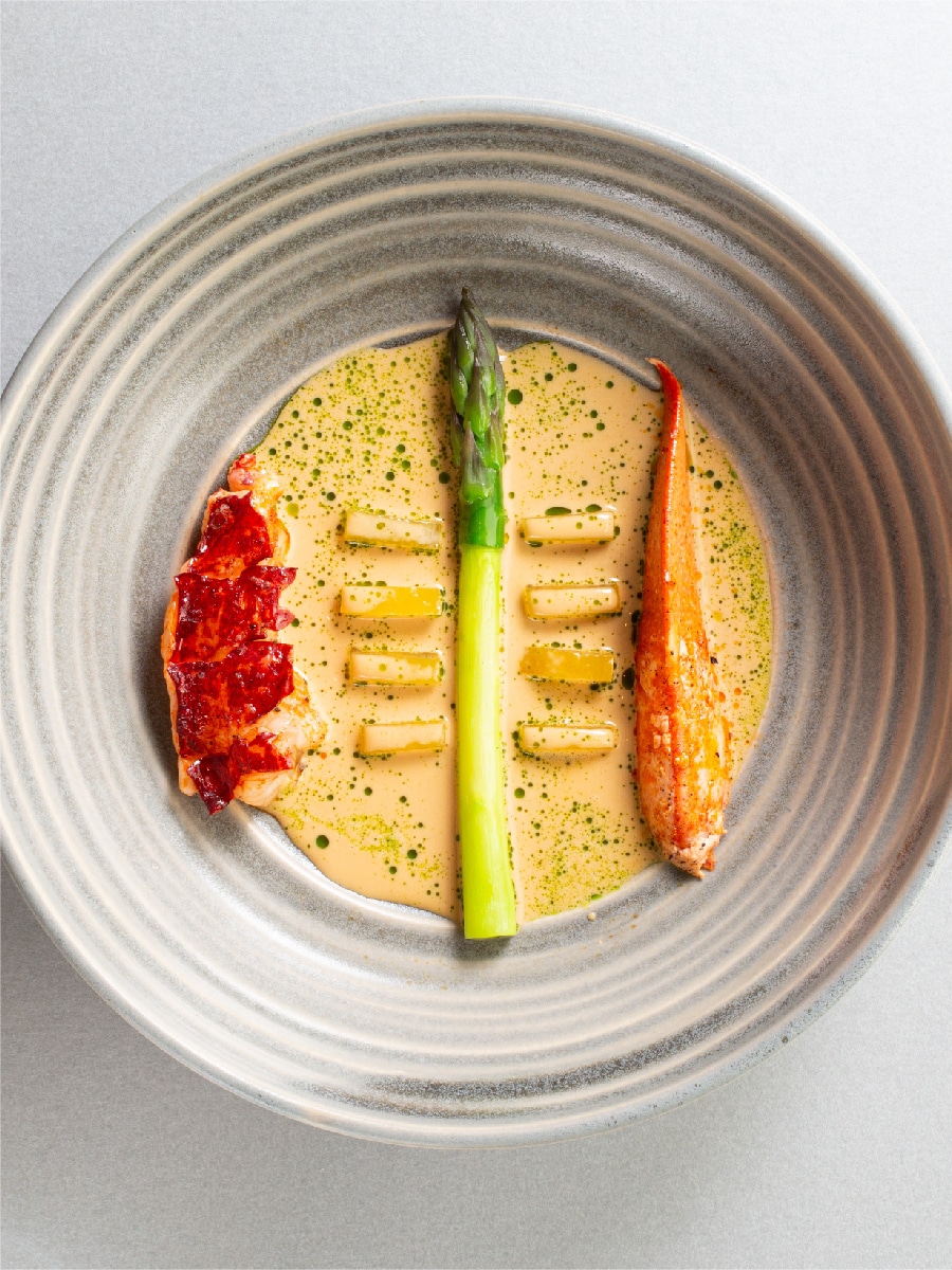 Cornish Lobster, Cooked Over Binchotan, Wye Valley Asparagus, Salted Lemon, Tahicain Vanilla, Lovage Over Head Sauce on Cornish Lobster, Cooked Over Binchotan, Wye Valley Asparagus, Salted Lemon, Tahicain Vanilla, Lovage Over Head Sauce on